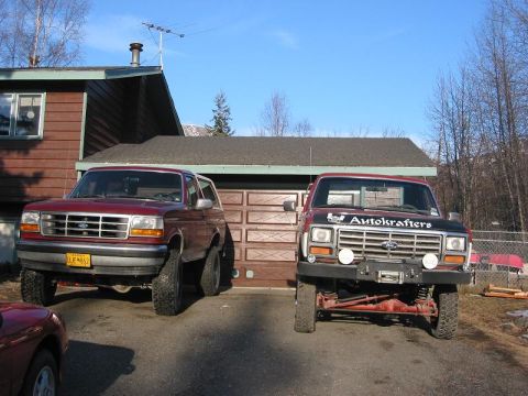 1985 Ford Bronco - Two Ford SUVs are parked in front of a residential garage on a sunny day.