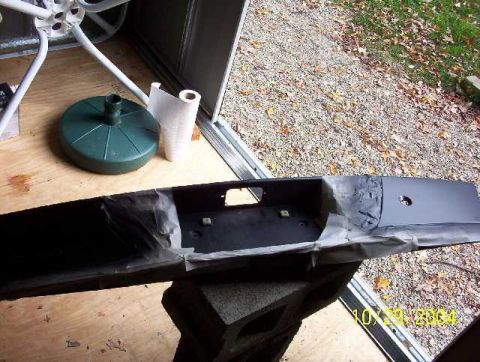 1999 Ford Crown Victoria - A car bumper is taped and prepared for painting, resting on cinder blocks outdoors.