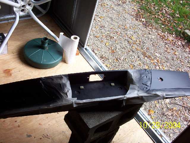 Black car bumper, taped for painting, resting on cinder blocks