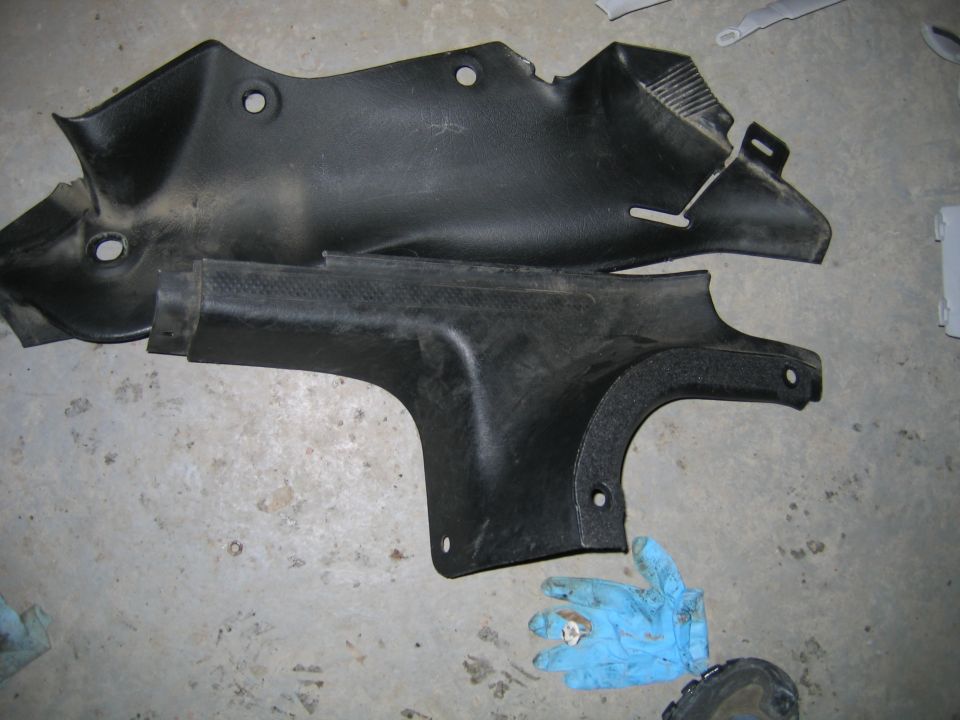 Two black plastic trim pieces on a concrete floor. A gloved hand is visible at the bottom right