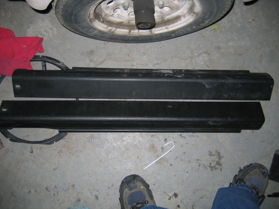 Two black plastic car door trim pieces laid on a concrete floor next to a tire