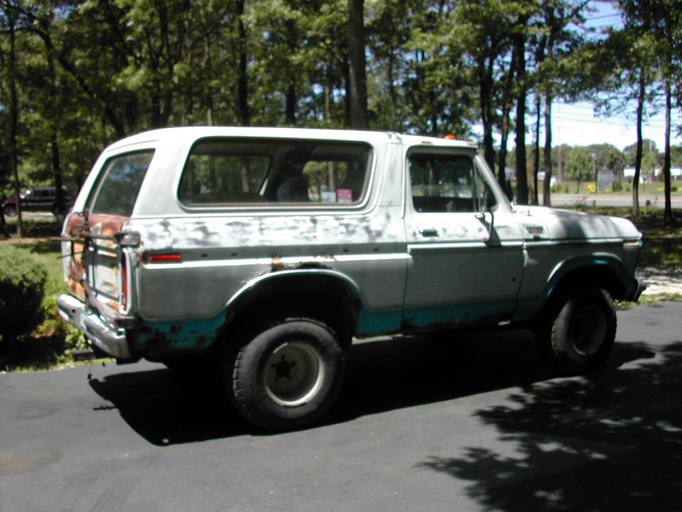 Faded white and teal Ford Bronco with rust, lift, and big tires in a driveway