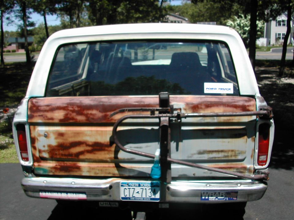 Rear tailgate of weathered Ford Bronco with rust streaks, tire carrier, and NY plate CIZ-7134