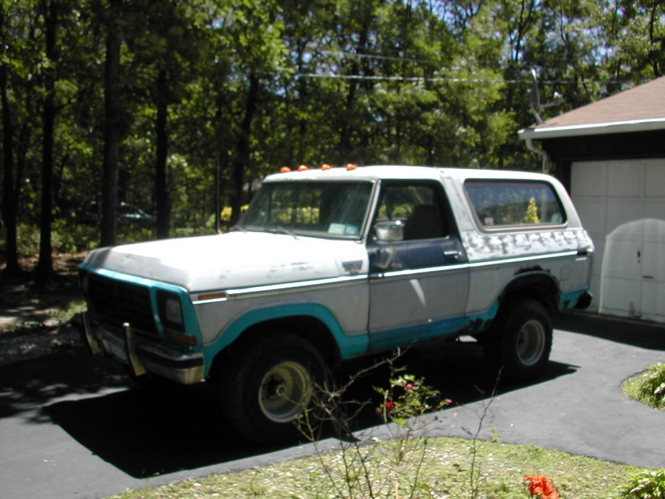 Lifted white and teal Ford Bronco with roof lights parked on driveway by garage