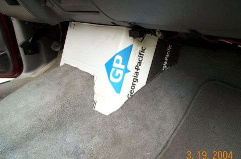 1996 Ford Bronco - Interior passenger footwell of a vehicle showing gray carpet and a folded Georgia-Pacific cardboard box with a blue 'GP' logo tucked under…