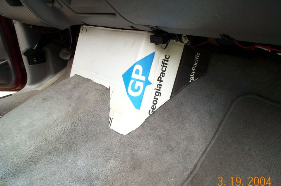 Passenger footwell with gray carpet and Georgia-Pacific cardboard under the dash