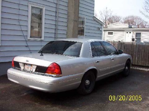 1999 Ford Crown Victoria - A silver sedan is parked in a driveway next to a residential building.