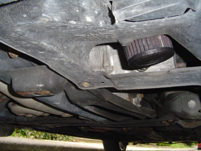 Underbody view showing an oil filter through an opening in a plastic splash shield