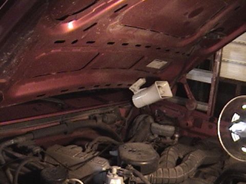 1994 Ford Bronco - The engine bay of a vehicle is shown with the hood open, revealing the engine and a mounted horn. The red hood interior is also visible.