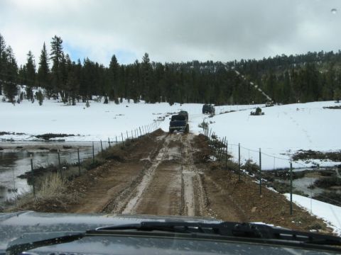 1985 Ford Bronco - Several SUVs navigate a challenging muddy and snowy track through a wooded area.