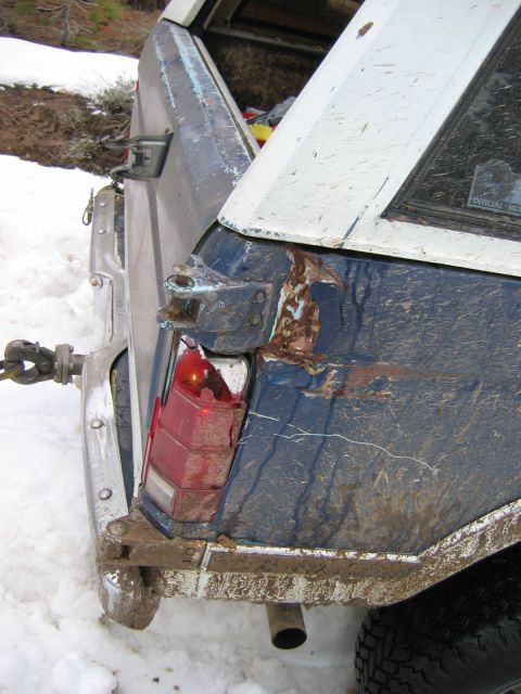 1985 Ford Bronco - The rear of a mud-covered SUV shows damage and rust, with a tow strap attached in a snowy environment.