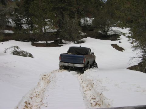 1985 Ford Bronco - A blue pickup truck navigates a snowy track in a wooded area.
