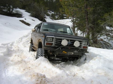 1985 Ford Bronco - This 1980s Ford Bronco navigates a snowy, off-road path with trees on either side.