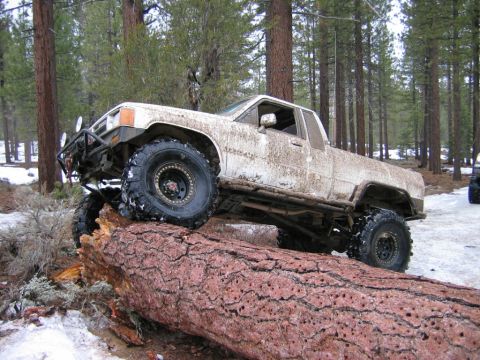 1985 Ford Bronco - Modified pickup truck navigating an obstacle in a snowy forest environment.