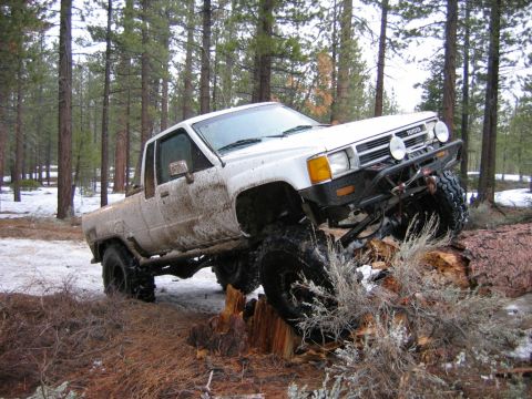 1985 Ford Bronco - This modified Toyota pickup truck is navigating a challenging off-road course in a wooded area with snow on the ground.