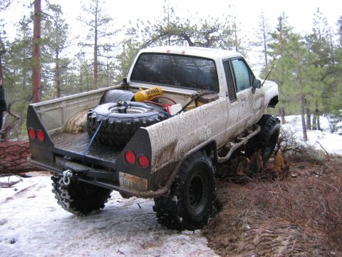 1985 Ford Bronco - This heavily modified white pickup truck features oversized tires and a custom flatbed, seen navigating a snowy and muddy terrain.