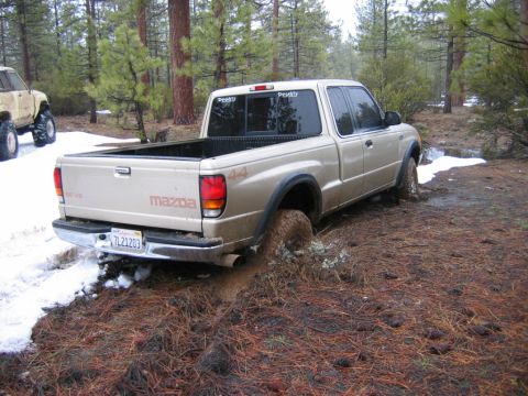 1985 Ford Bronco - Mazda pickup truck stuck in mud off-road, with another vehicle in the background.