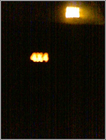 1993 Ford Bronco - Night shot of a darkened dashboard with an illuminated amber "4X4" indicator lamp glowing, and a brighter backlit display above it.