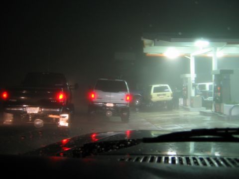1985 Ford Bronco - Multiple vehicles are seen at a gas station in the rain at night.