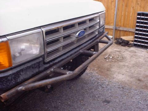 1988 Ford Bronco - Angled close-up of the front corner of a white Ford truck fitted with a home-built bare steel tube bumper with angled wing supports and no…