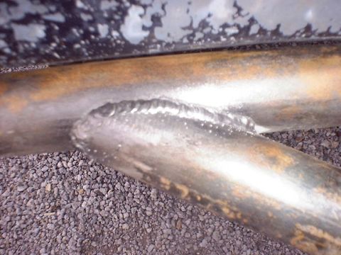 1988 Ford Bronco - Tight close-up of a stacked-dime weld bead joining two round steel tubes of a fabricated bar or bumper, the bare metal already showing surf…