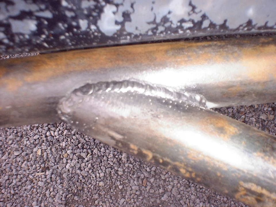 Close-up of weld bead joining two steel tubes on a fabricated bar over gravel