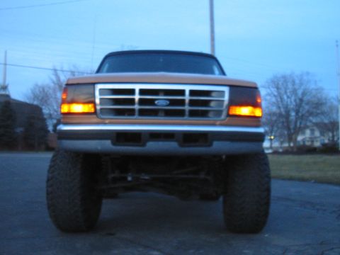 Front view of a lifted 1995 Ford Bronco with orange paint and a chrome grille