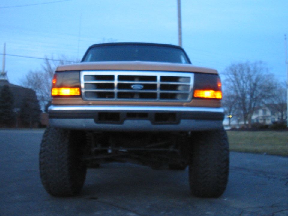 Front view of a lifted 1995 Ford Bronco with orange paint and a chrome grille
