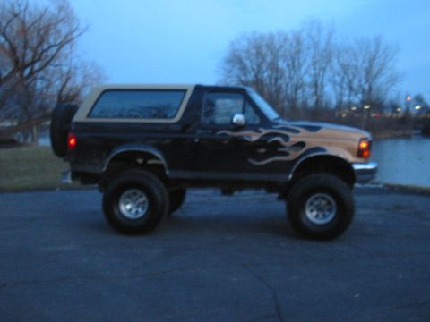 Lifted black and tan Ford Bronco with flame decals, spare tire on back