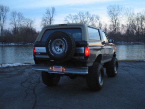 Dark gray and tan Ford Bronco with a rear-mounted spare tire, lifted suspension, and aftermarket wheels parke…
