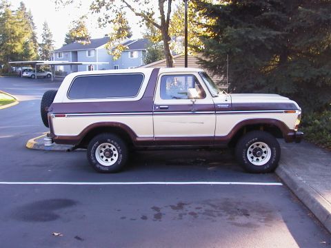 1979 Ford Bronco - A two-tone brown and cream 1970s Ford Bronco full-size SUV shown in full right-side profile, parked in an asphalt lot with a spare tire mou…