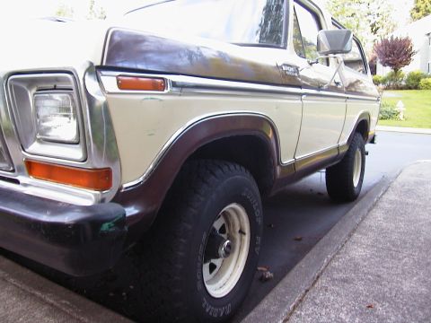 1979 Ford Bronco - Close low-angle view of the left front corner of a two-tone brown-over-cream late-1970s Ford Bronco, showing the chrome grille edge with re…