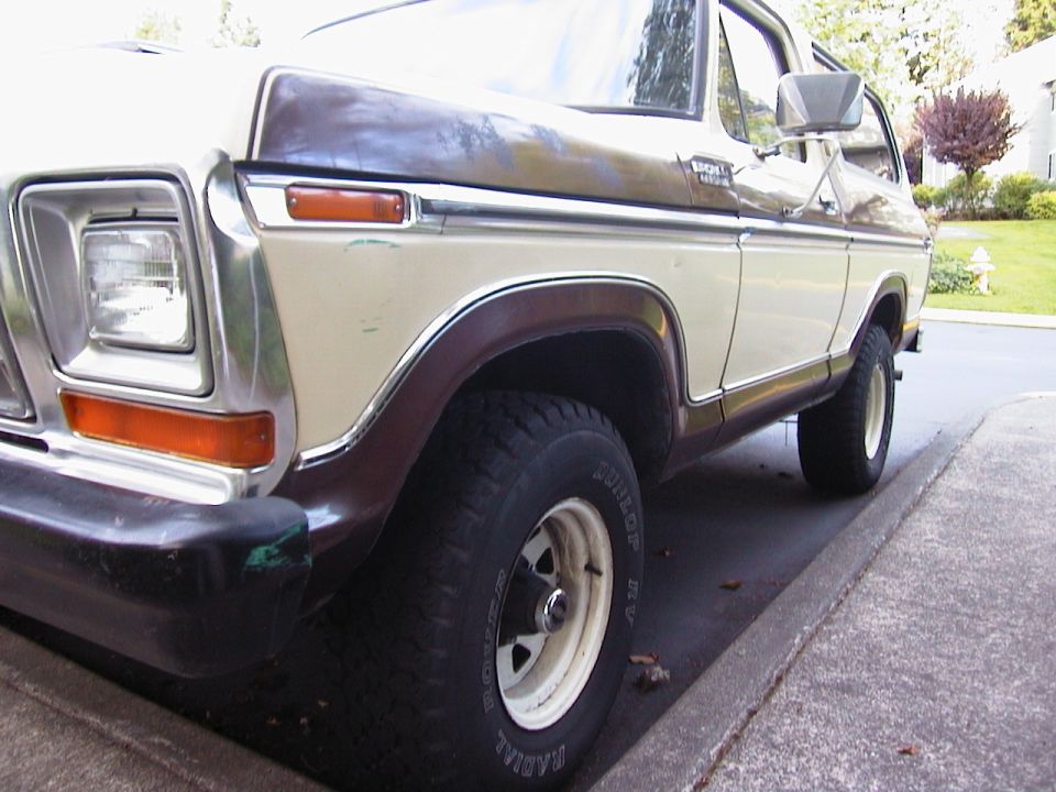Left front corner of a brown and cream 1970s Ford Bronco with white-letter tire on white steel wheel
