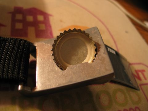 1995 Ford Bronco - A metal bottle opener, part of a black strap buckle, is shown with a bottle cap stuck inside its opening.