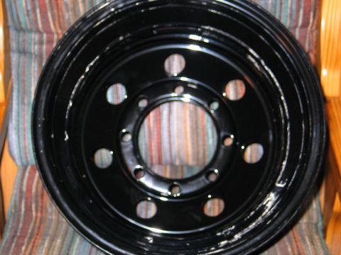 1989 Ford F-150 - A black steel wheel is shown close-up, resting on a striped cushion with wooden chair arms visible.