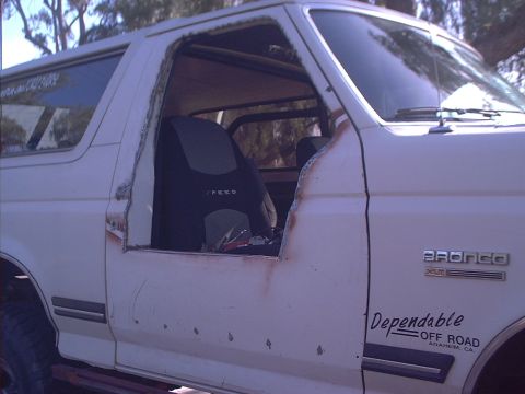 1990 Ford Bronco - Side view of a white Ford Bronco with the driver's door skin cut away above the beltline, leaving a rough raw-metal opening and exposing th…