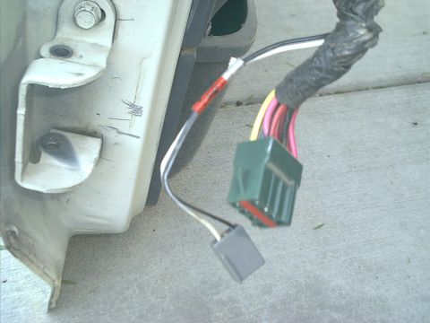 1990 Ford Bronco - Close-up of an unplugged wiring harness on concrete beside a white painted body panel edge, showing a green multi-pin connector with yellow…