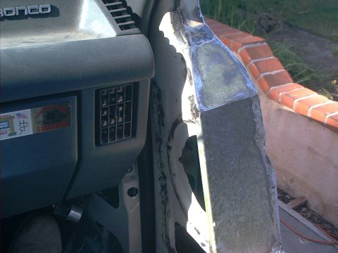 1990 Ford Bronco - Close-up of a cut-away door pillar and cowl area on a white Ford Bronco during body surgery, with raw sheet-metal edges, seam sealer and ba…