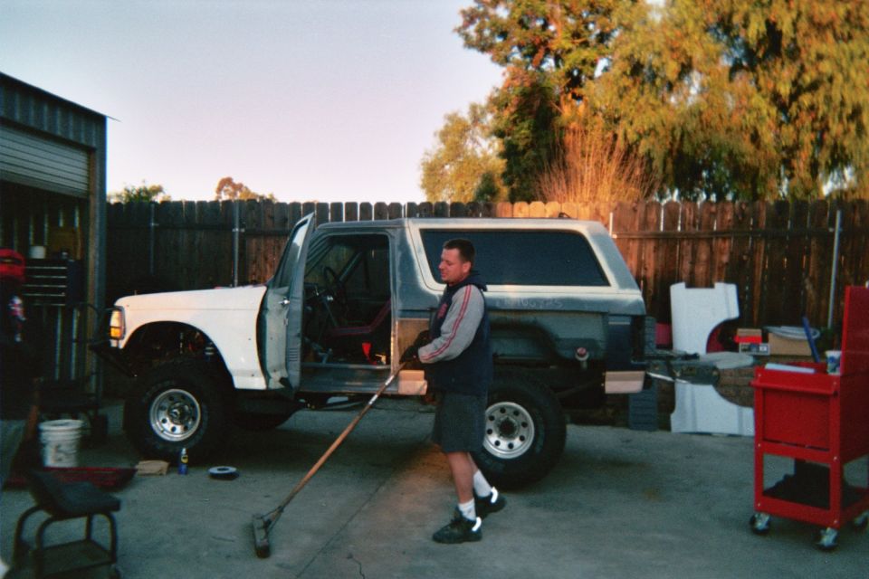 Man working on a white full-size Bronco with the door open in a backyard