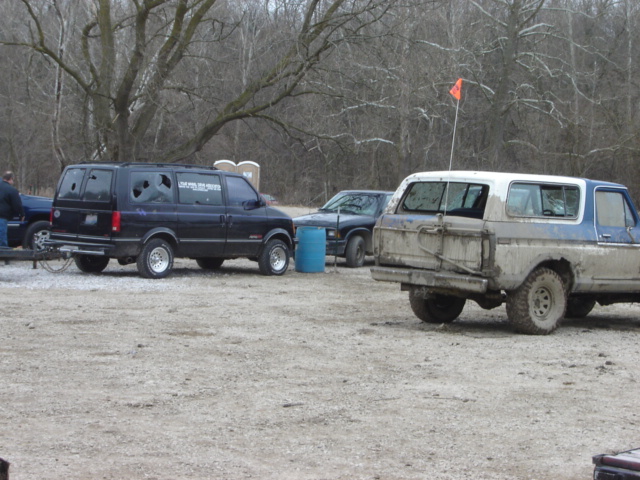 Muddy Ford Bronco, looks like an 80s model, parked next to a black van and a dark pickup truck