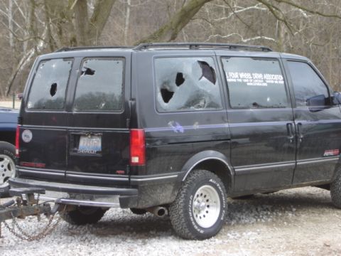 1992 Ford Bronco - A black van with multiple broken windows is parked outdoors.