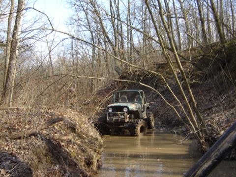 1992 Ford Bronco - A modified Jeep navigates a water obstacle on a wooded trail.