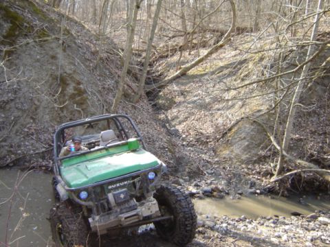 1992 Ford Bronco - Off-road vehicle navigates a rocky creek bed in a wooded environment.