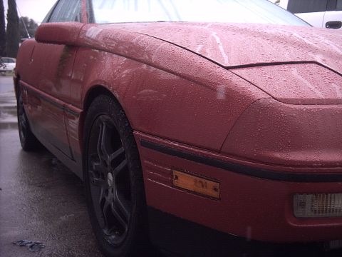1989 Ford Probe - A red 1989 Ford Probe is shown from the front three-quarter view, covered in water droplets.