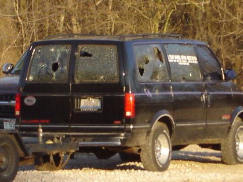 1992 Ford Bronco - This black van has multiple broken windows and is parked next to another vehicle.