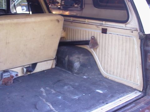 1979 Ford Bronco - Passenger-side rear interior of a full-size SUV shot from the open tailgate, showing a tan pleated vinyl quarter trim panel and folded benc…