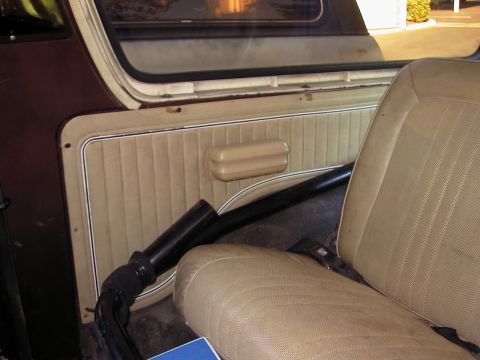 1979 Ford Bronco - Interior shot of a truck's passenger-side rear quarter, with a tan pleated vinyl trim panel and armrest below a sliding side window. A blac…