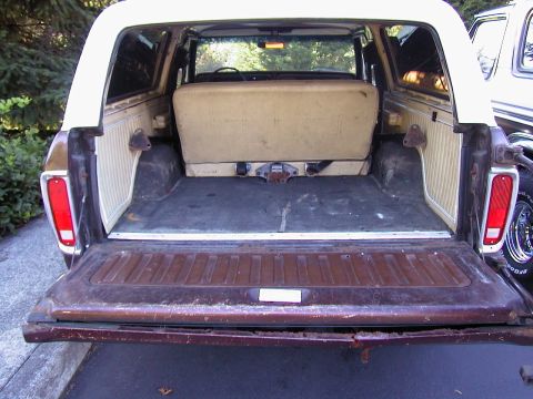 1979 Ford Bronco - Rear view of a 1979 Ford Bronco with the tailgate lowered, showing the cargo area with a folded tan/beige rear bench seat, weathered gray c…