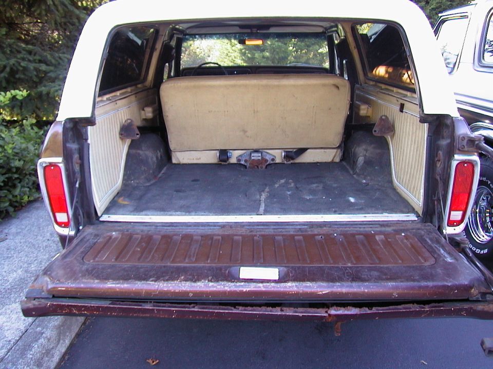 Rear cargo area of Ford Bronco with tailgate down, tan folded bench seat and maroon panels