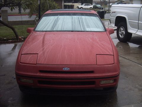 1989 Ford Probe - A red 1989 Ford Probe sits in the rain, its windshield streaked with water.
